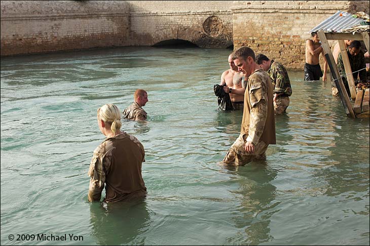 Sweating and dusty, the soldiers wade into a chilly river running through camp, uniforms and all.