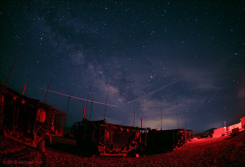 Styrkers bathed in the glow of the rig, under the Milky Way.  The bright streak is from an unmanned aircraft.